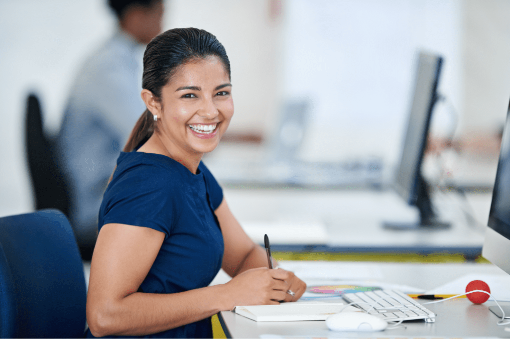 A smiling woman sitting at a desk in front of a computer.