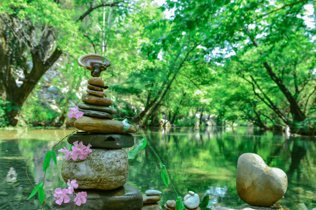 A mesmerizing stack of rocks and vibrant flowers adorning a serene river, embodying the concept of the Wheel of Life.
